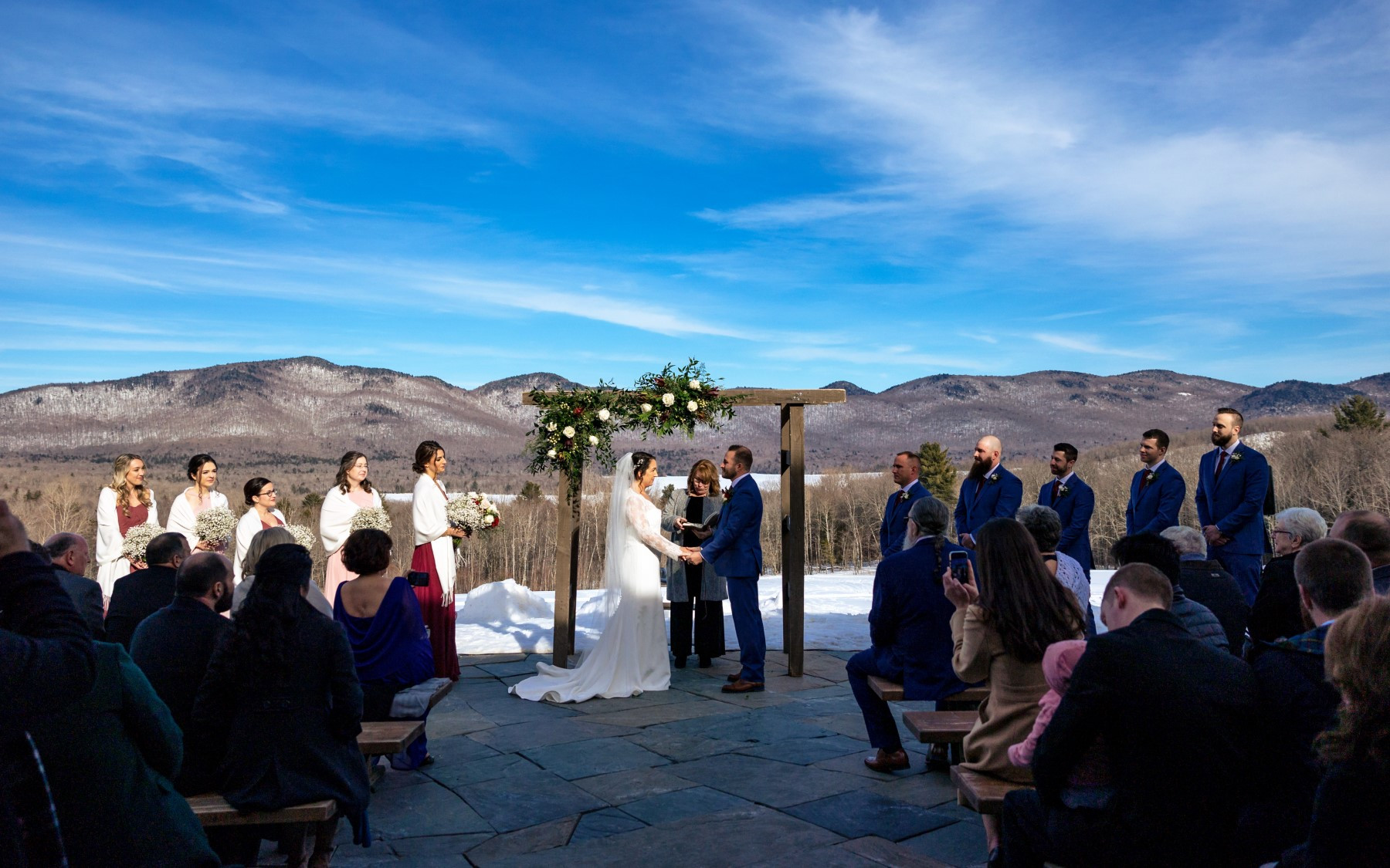 winter wedding on terrace with floral design, featuring bride and groom underneath the arbor, in front of mountains