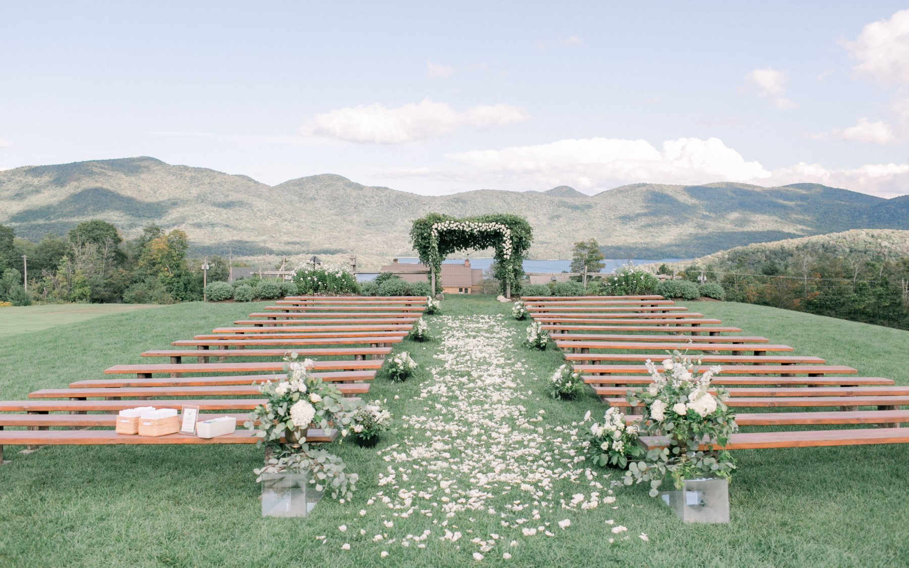 Wedding Knoll in Spring, featuring floral designs in front of farmhouse benches, petals scattered between, all in front of Green Mountains.