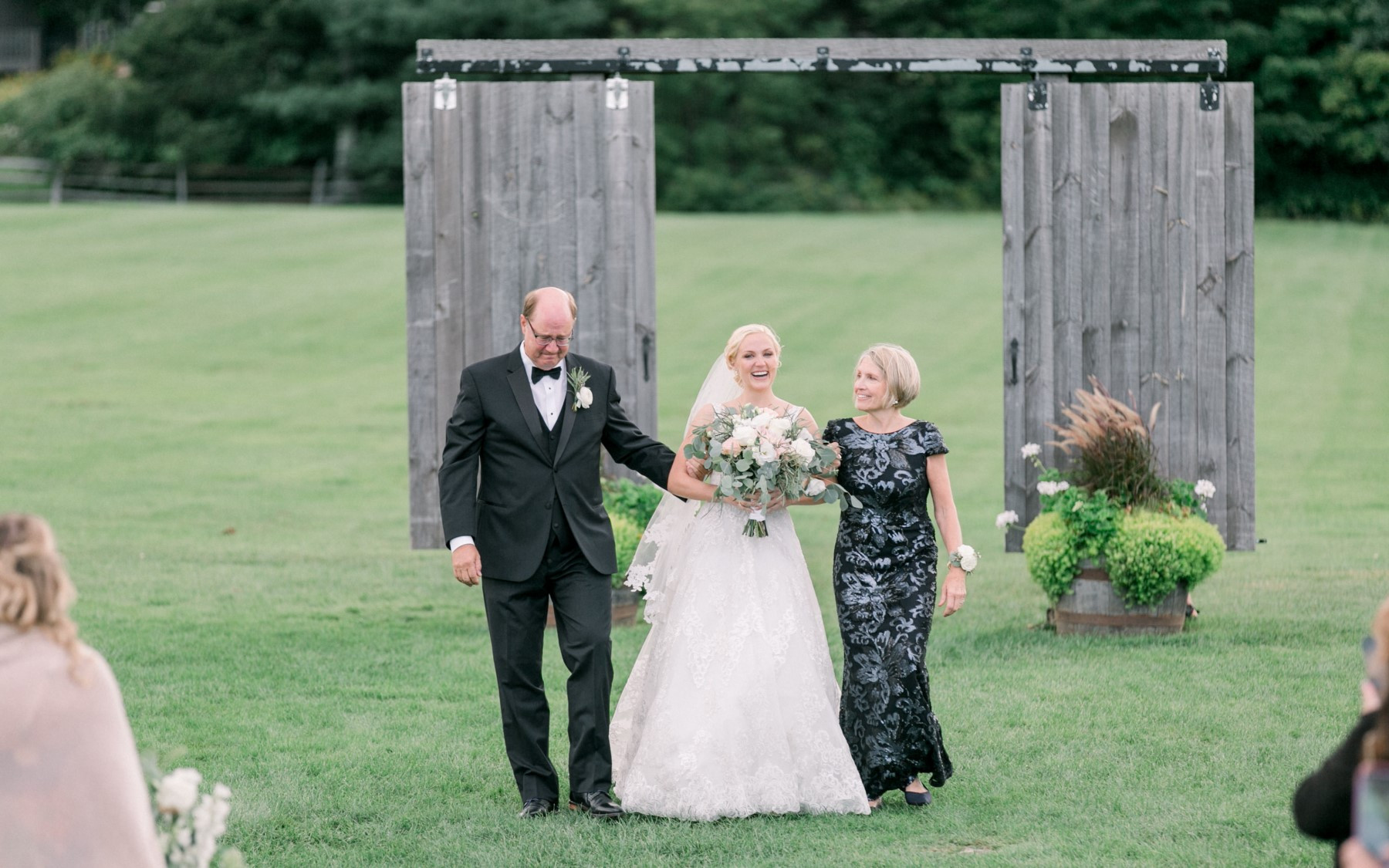 Bride with father and mother on either side, walking through Barnhouse Doors.