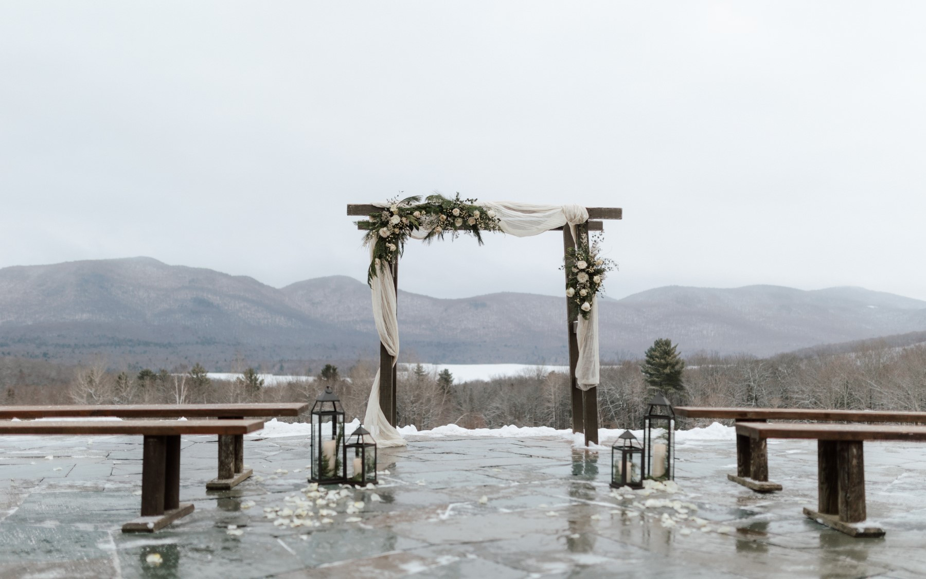 winter terrace designed for winter wedding featuring drapery and floral with black candle holders on the ground next to farmhouse benches
