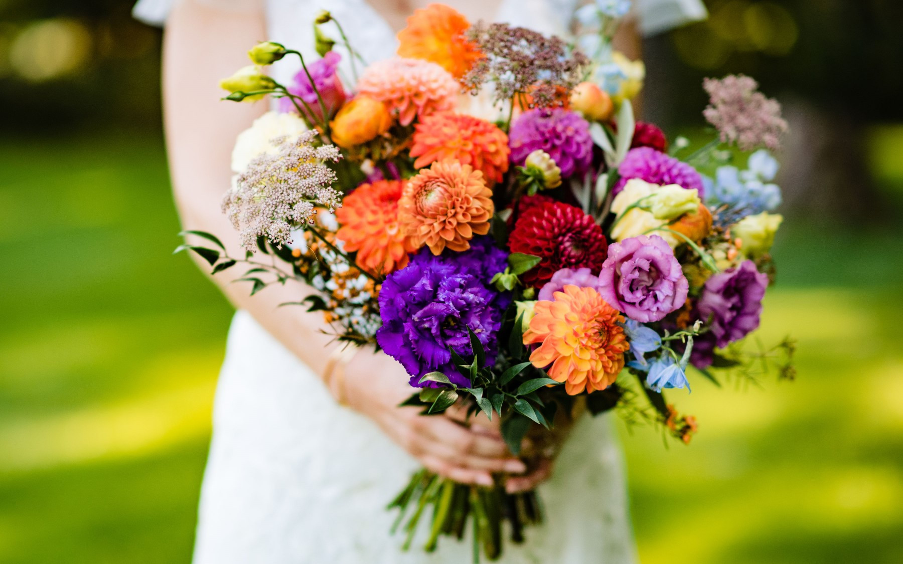 floral bouquet featuring red, orange, yellow, purple, blue, and white florals being held by bride.