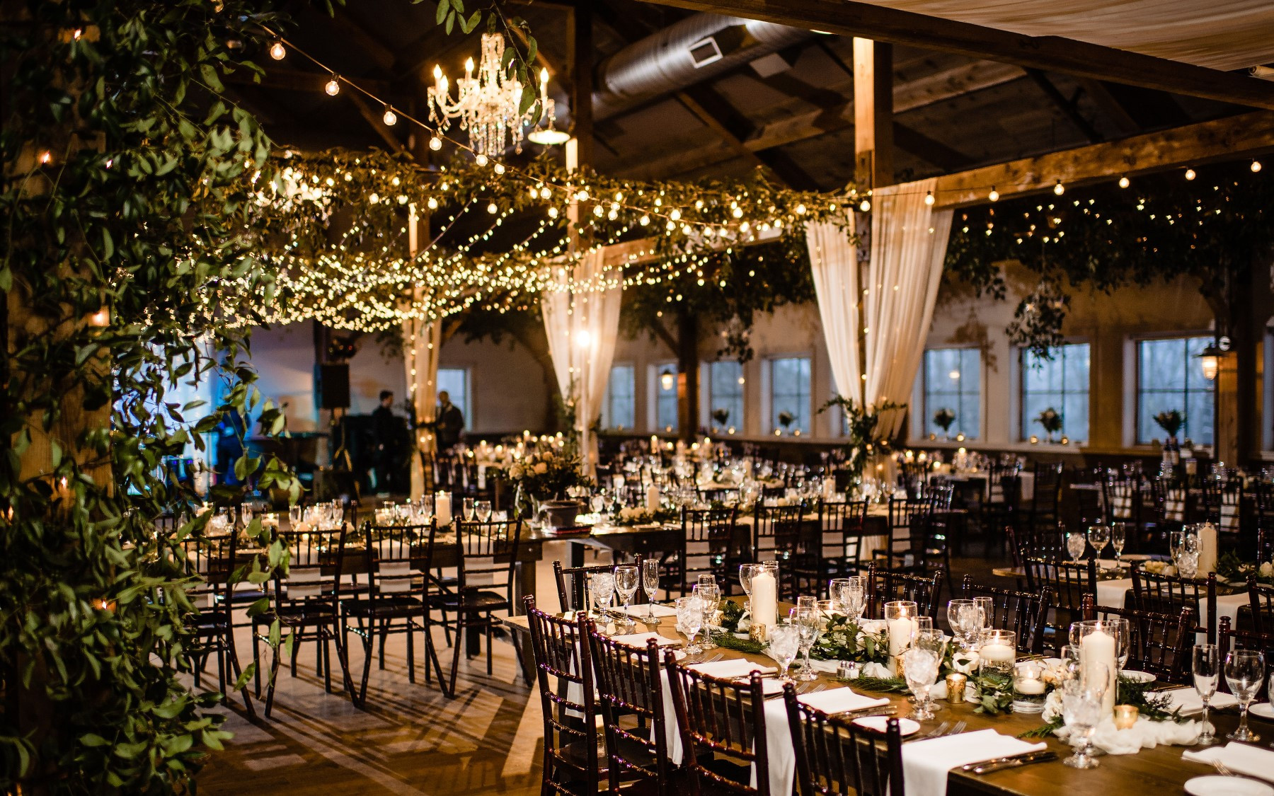event barn featuring greenery and lights with farmhouse tables.