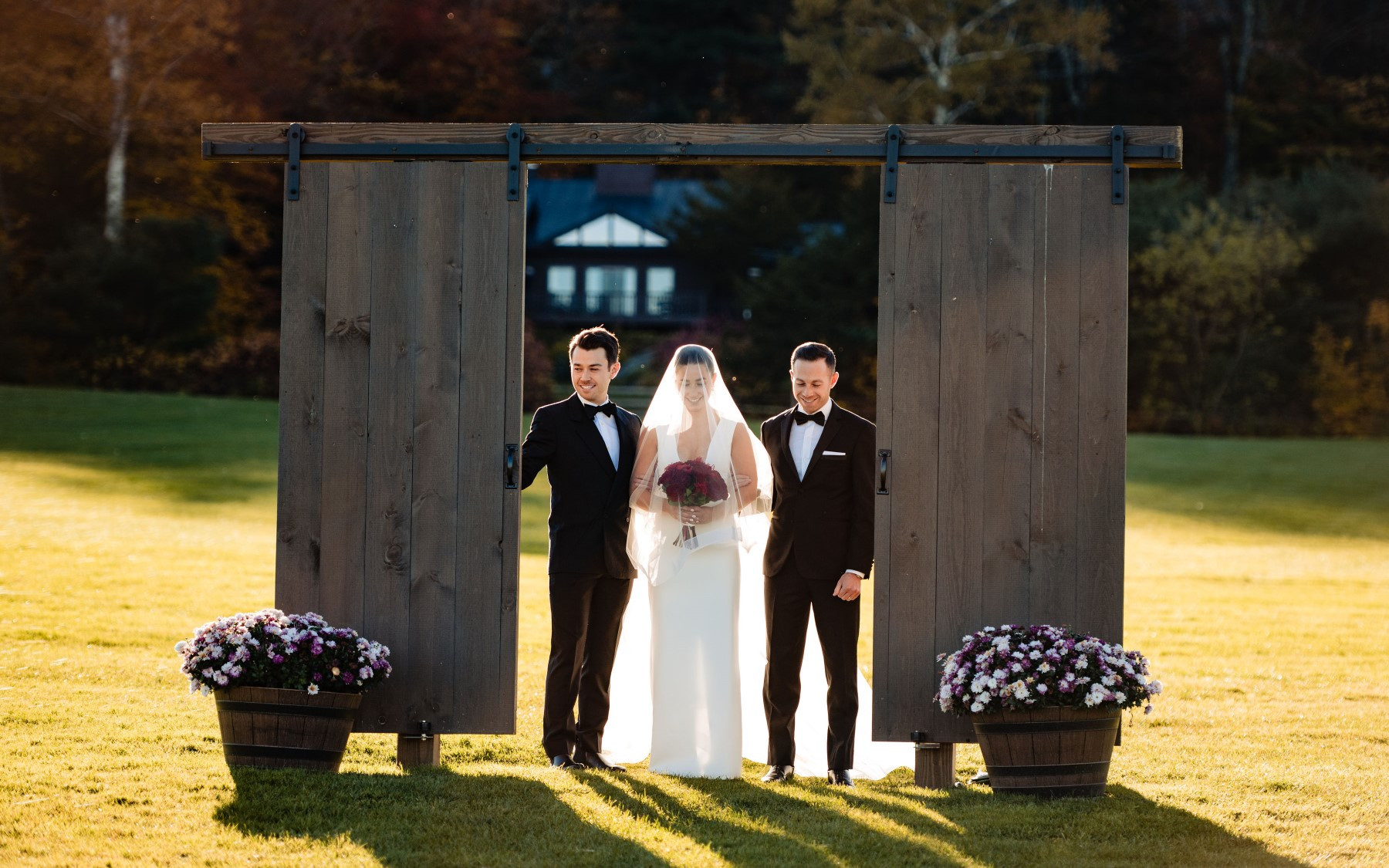barn doors being opened with bride and two groomsmen walking down wedding knoll.