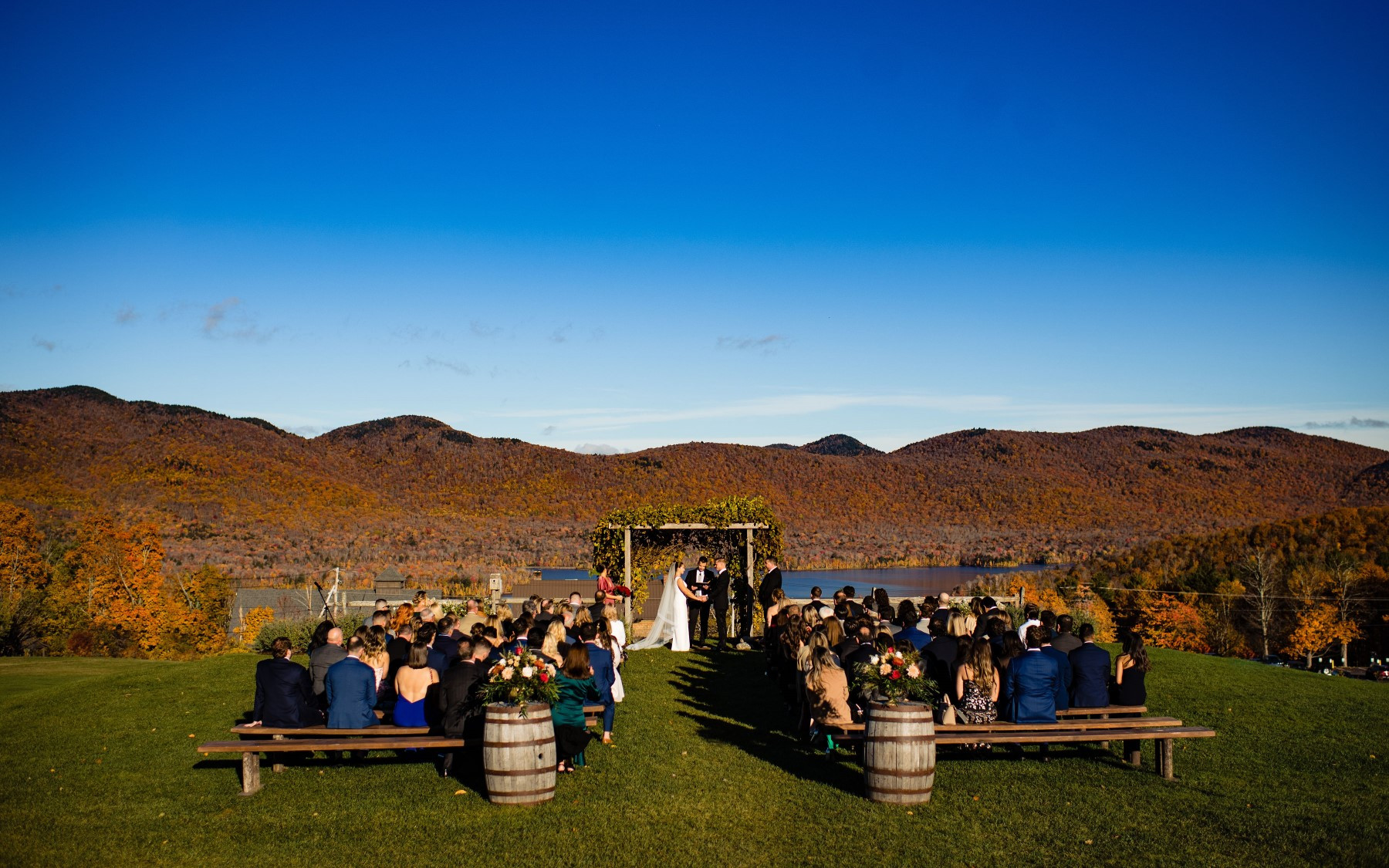 fall wedding knoll photo featuring guests on farmhouse tables, wedding knoll, and lake and mountains in the background.