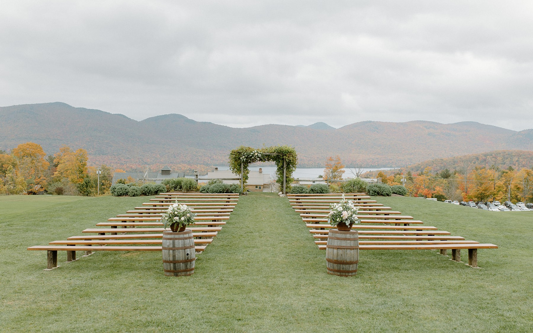 wedding knoll in fall with floral bouquets on top of whiskey barrels in front of farmhouse benches. background features lake and mountains with foliage.