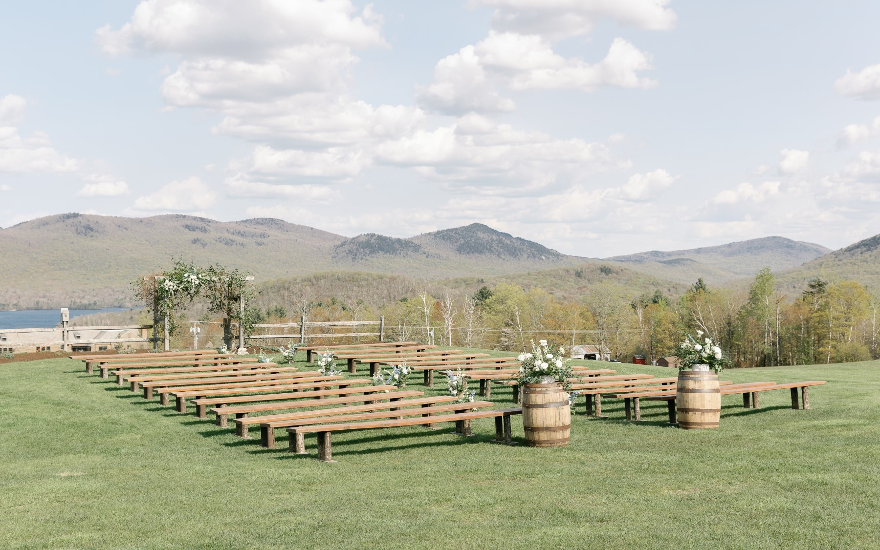 photo of wedding knoll with green mountains behind it and farmhouse benches in front with two whiskey barrels with flowers on top of them.