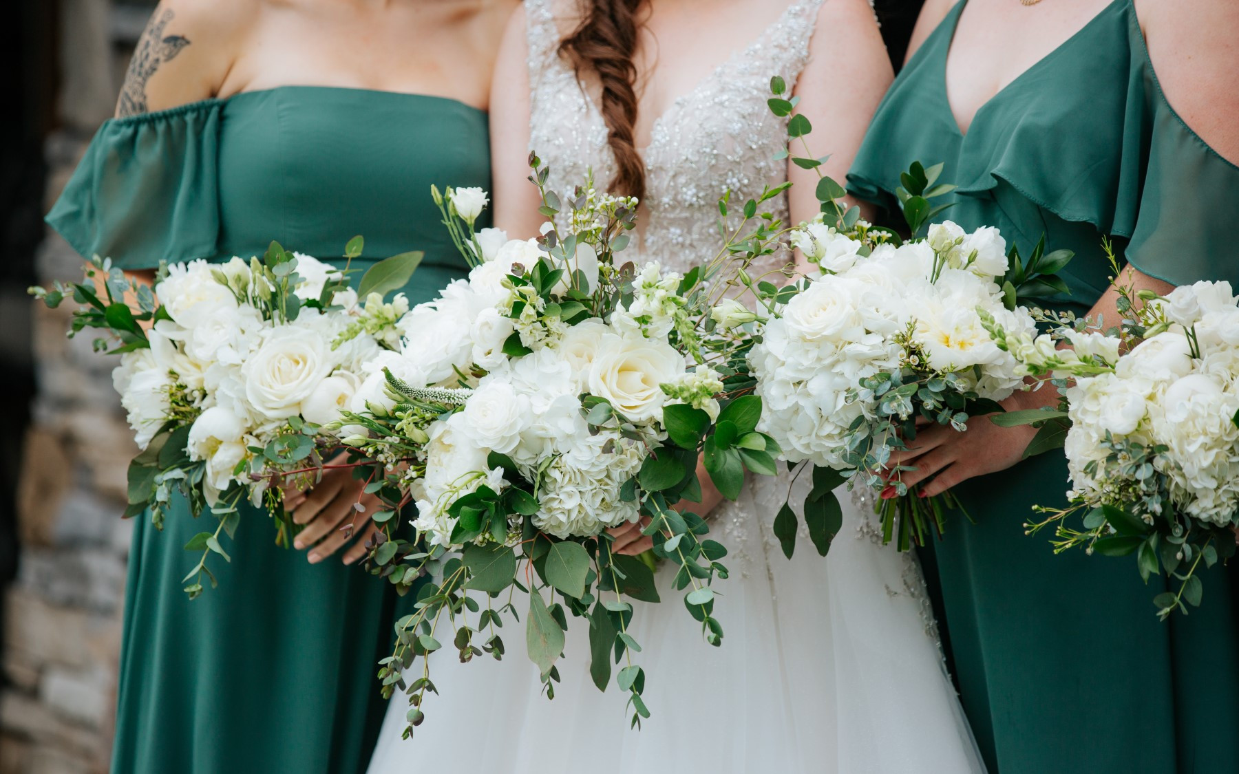bride in white and two bridesmaids in green dresses with large white and green bouquets in front of them