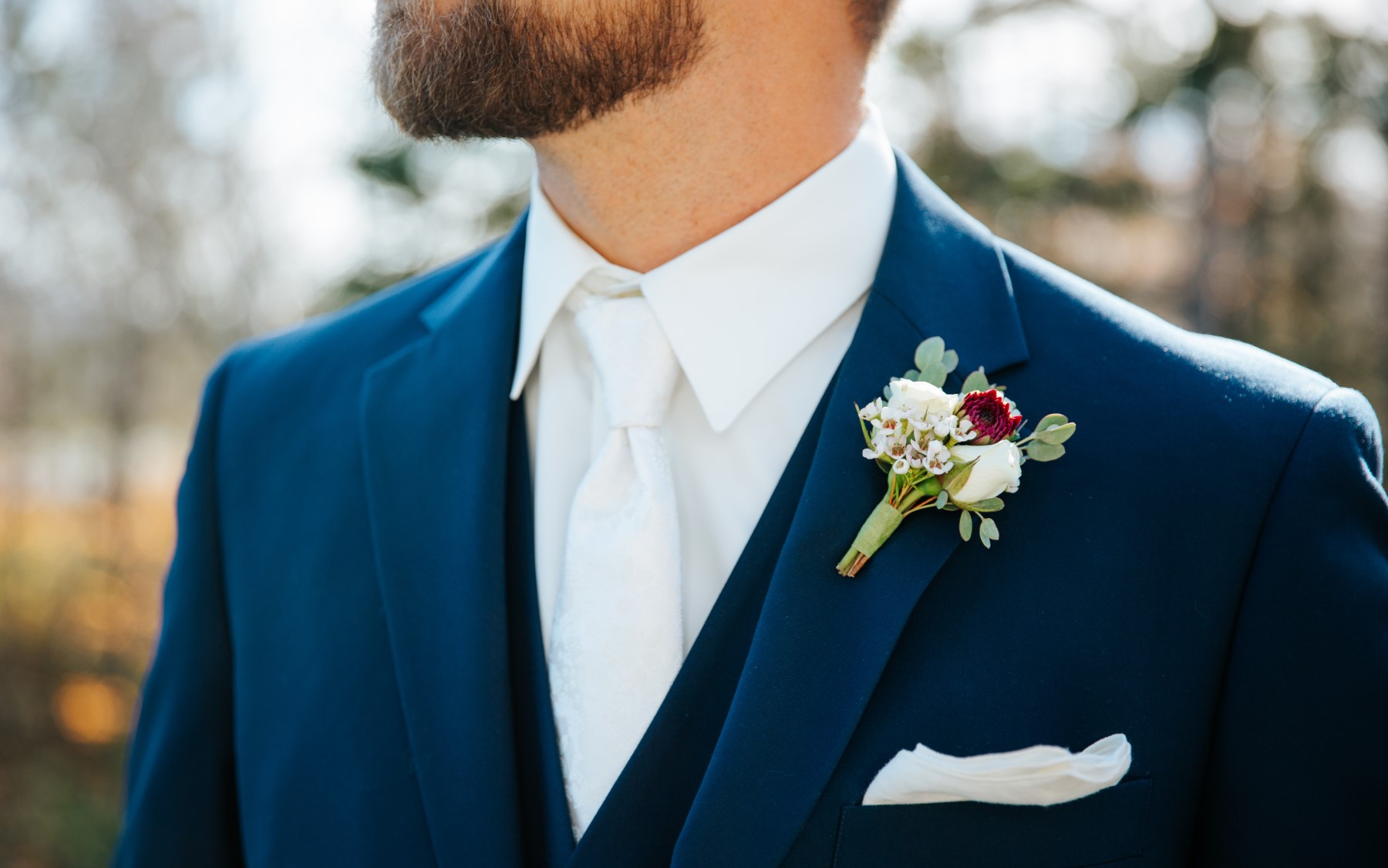 close up photo of groom in blue suit with white tie and small floral boutonierre