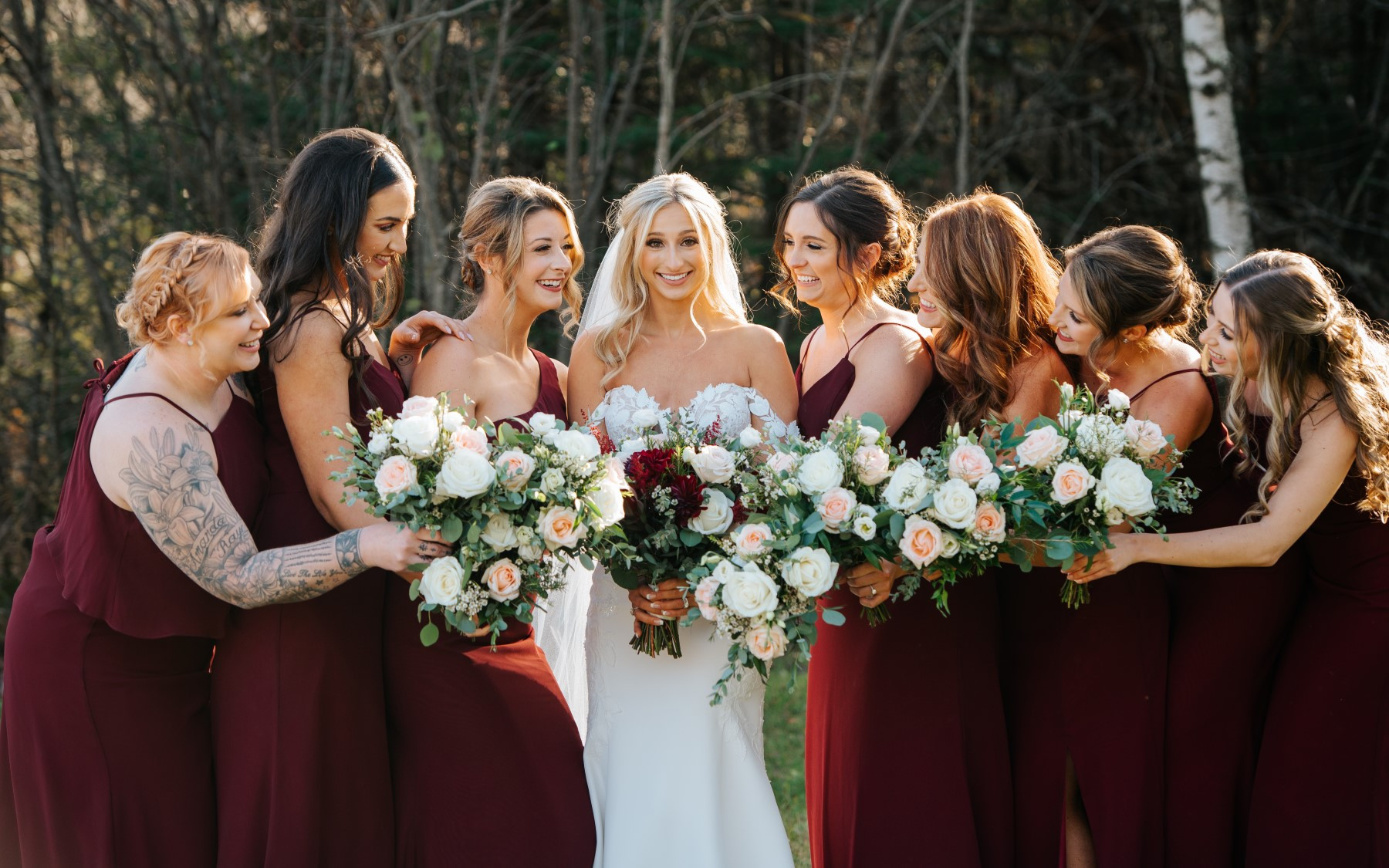bride and seven bridesmaids in red dresses leaning in holding bouquets. Bridal bouquet features red flowers while bridesmaid bouquets only have pink and white flora.