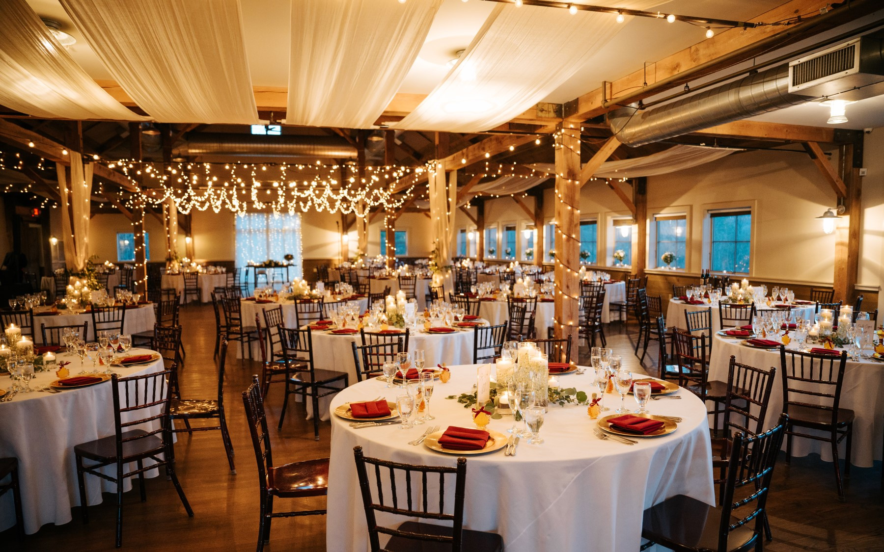 event barn for a reception dinner showcasing ribbons on the ceiling, and table rounds with red table cloths.