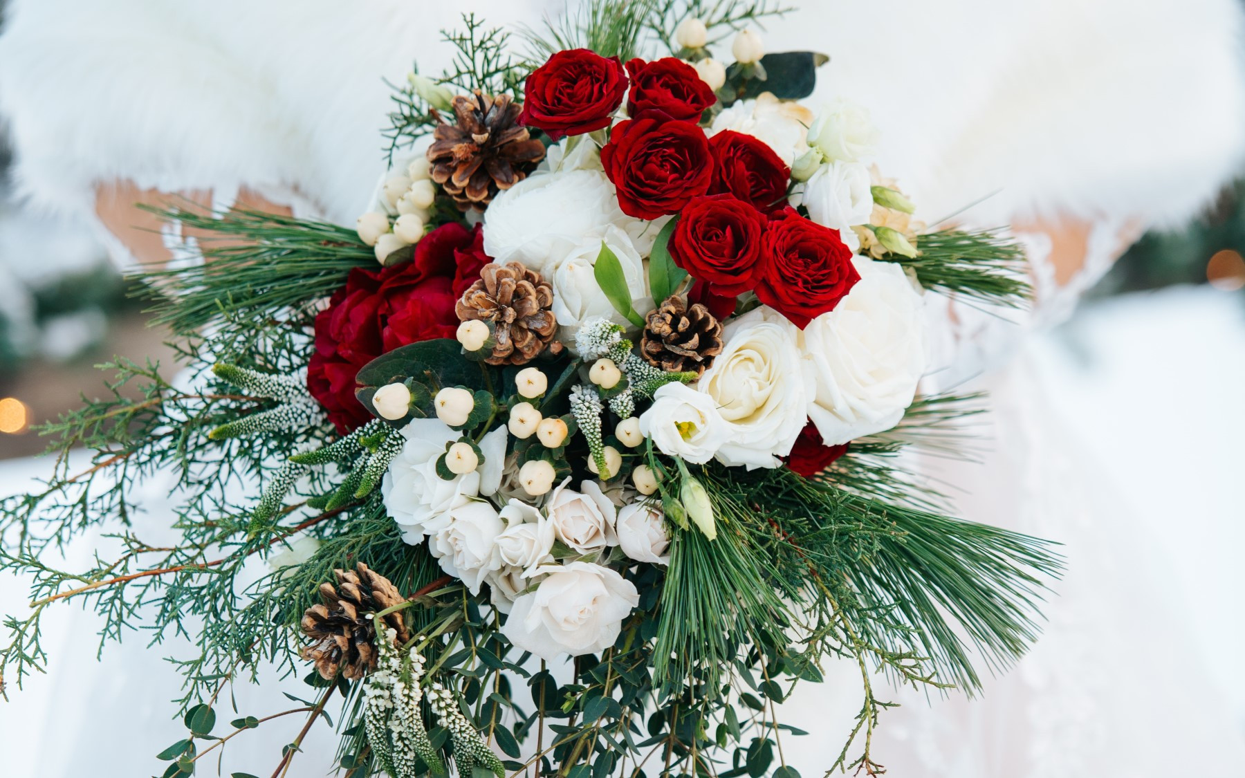 winter wedding bouquet featuring red roses, white roses, pinecones, pine, and other greenery.