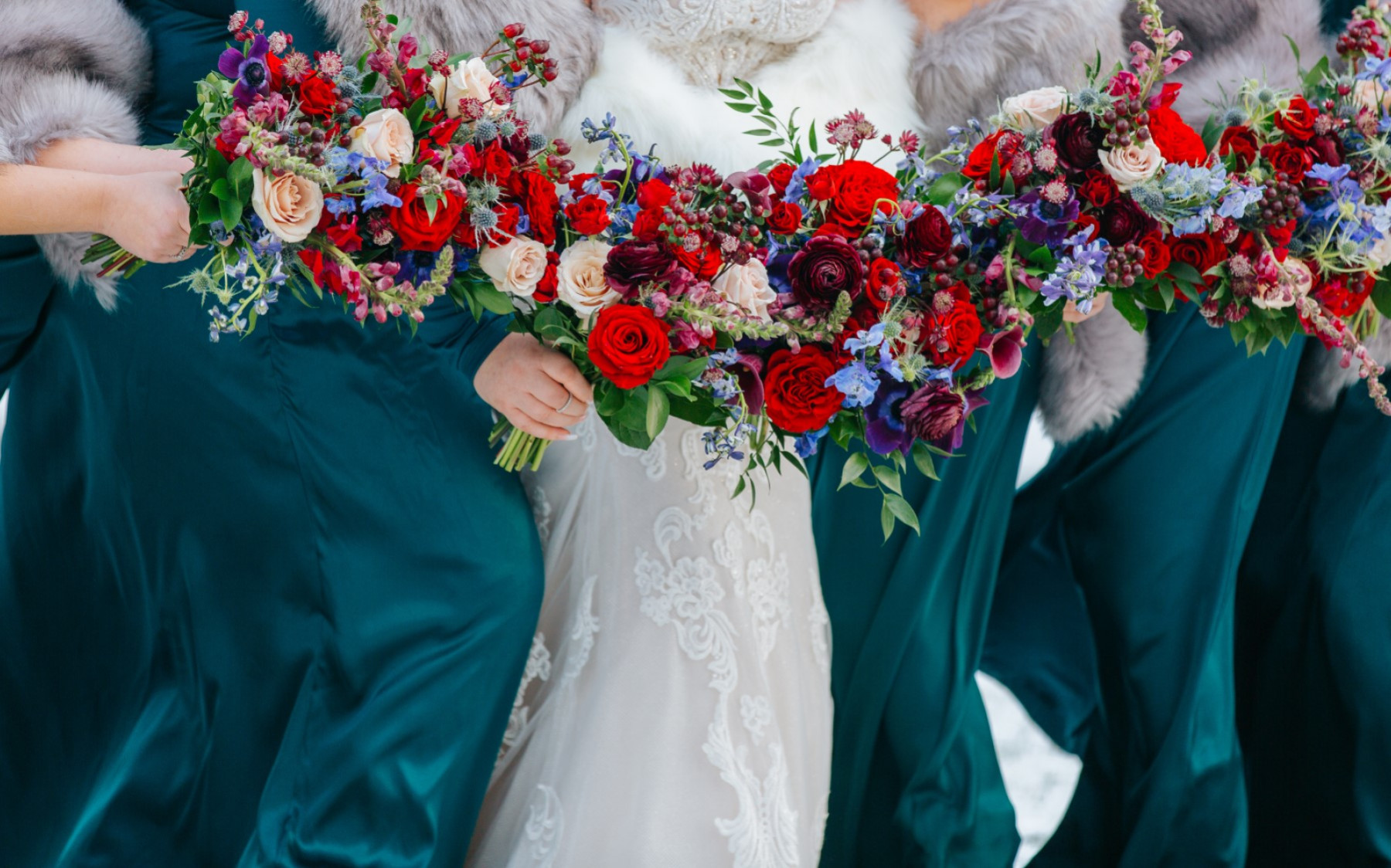 floral bouquets being held by bride and three other bridesmaids in teal. floral bouquets show red roses, pink, blue, and purple floral arrangements.