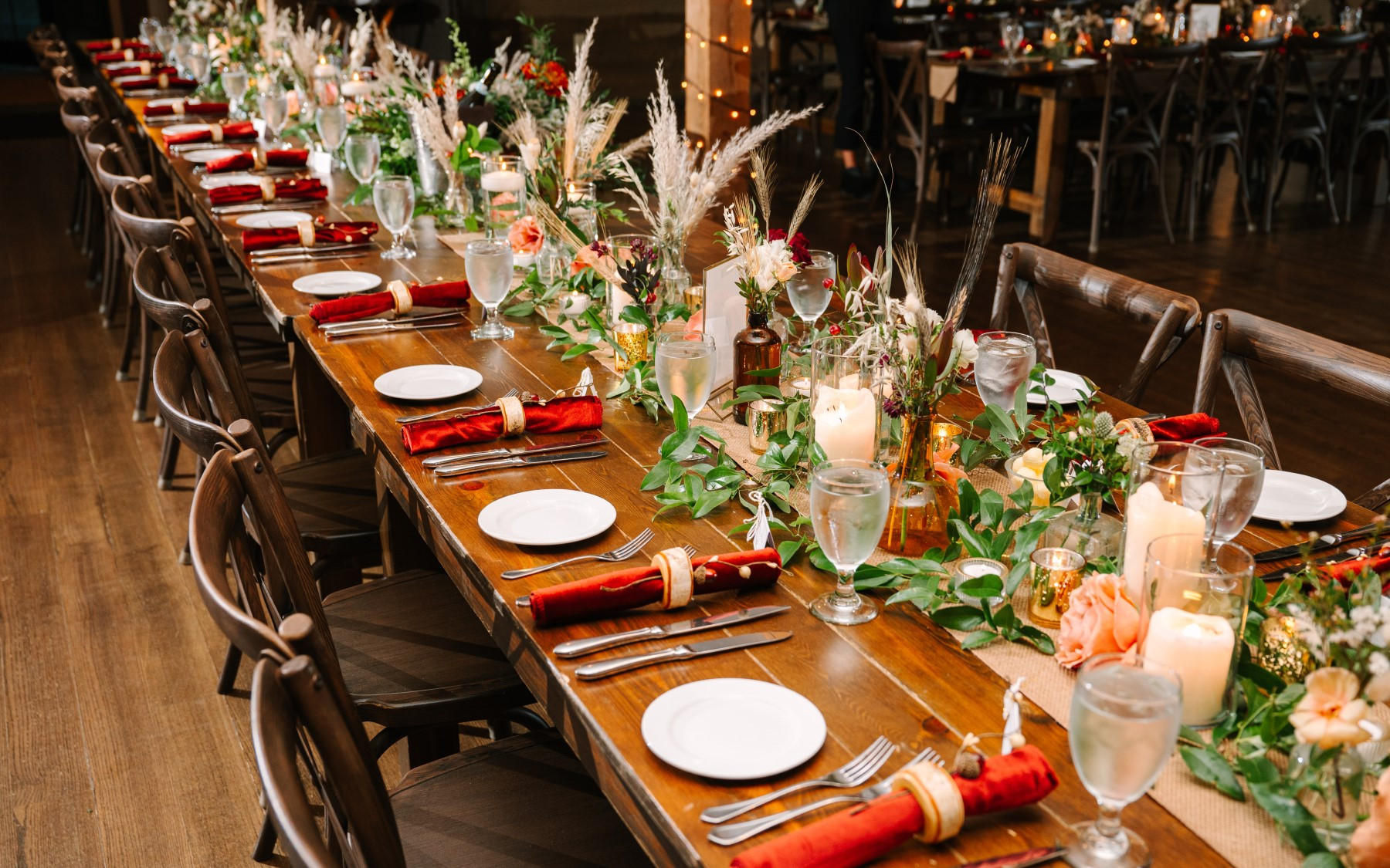 table setting for a fall wedding. napkiins are rolled in wooden napkin holders. table decor consists of pampas leaves, greenery, and candles in votives.