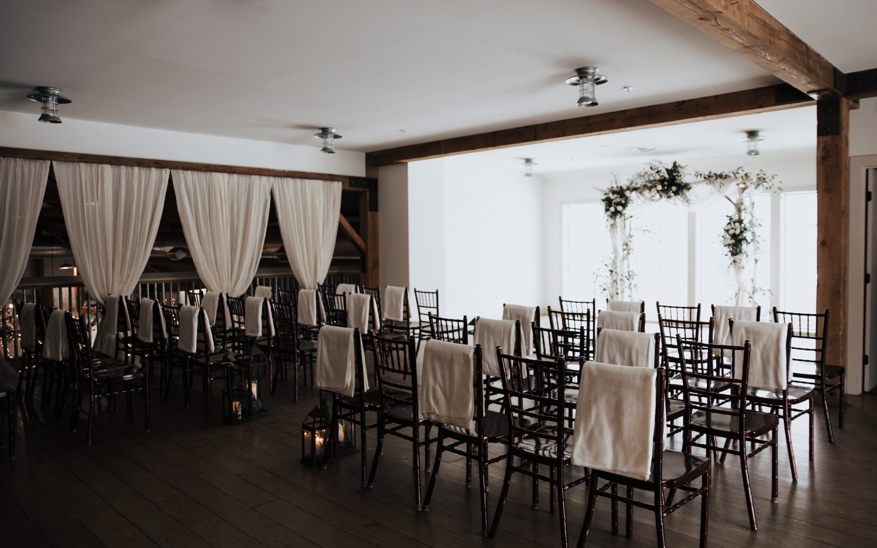 loft photo of wedding arbor with white floral designs and chairs placed with an aisle