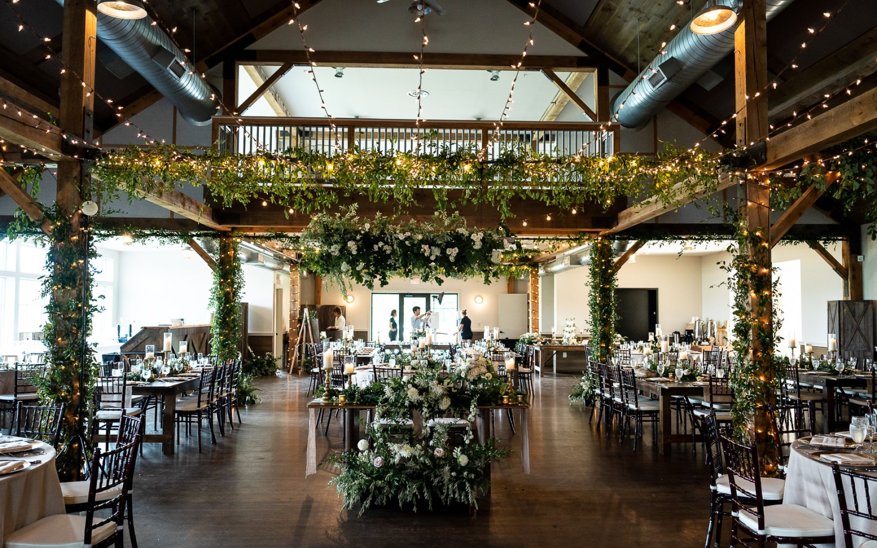 event barn photo featuring greenery on ceiling and rafters with the sweetheart table centered.