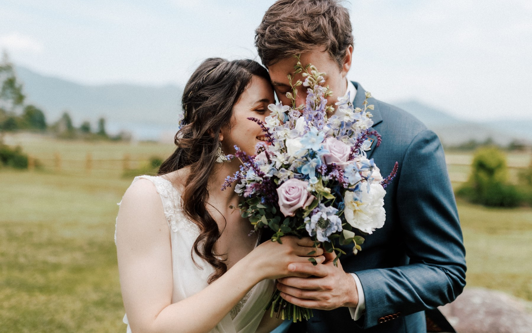 bride and groom hiding faces behind floral arrangement with blue and purple floweres.