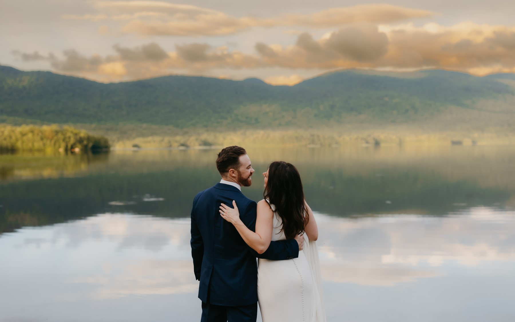 bride and groom overlooking summer lake with green mountains in background