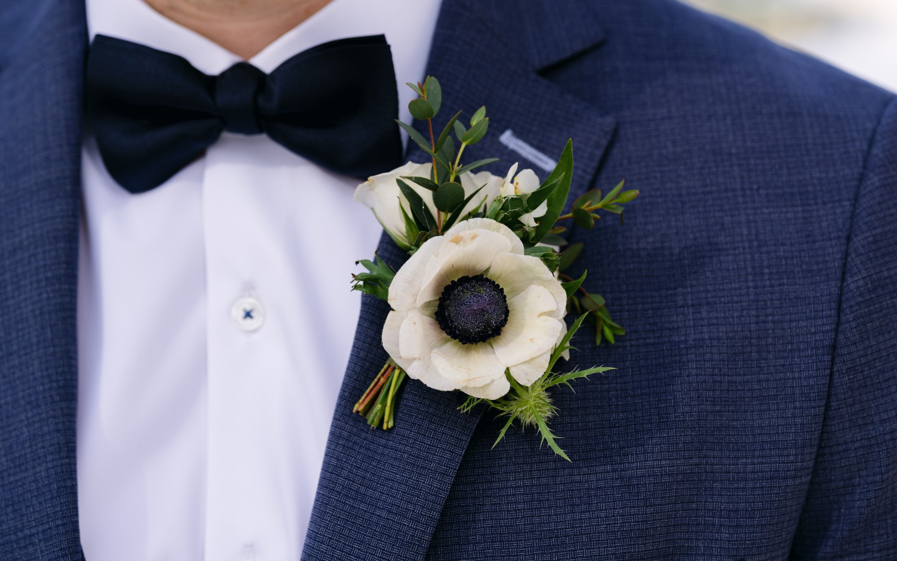 close up of boutonierre on groomsmen in blue tuxedo and bowtie.