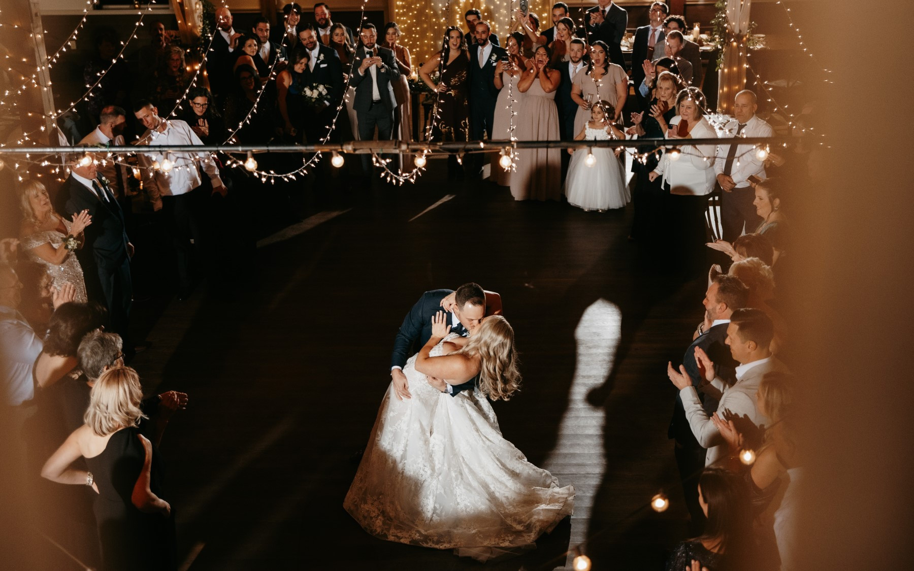 bride and groom kissing underneath cafe lights in event barn