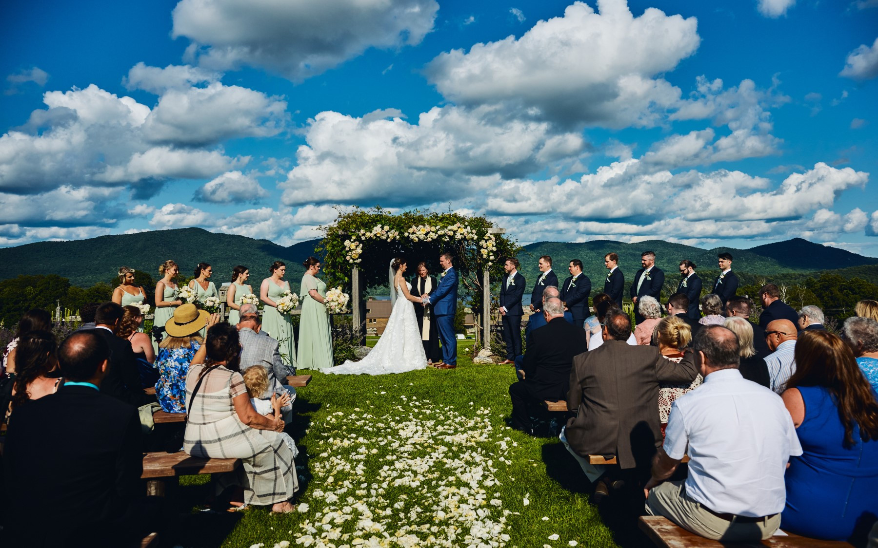 wedding knoll in the summer featuring bridesmaids in green dresses and grooms in blue suits.