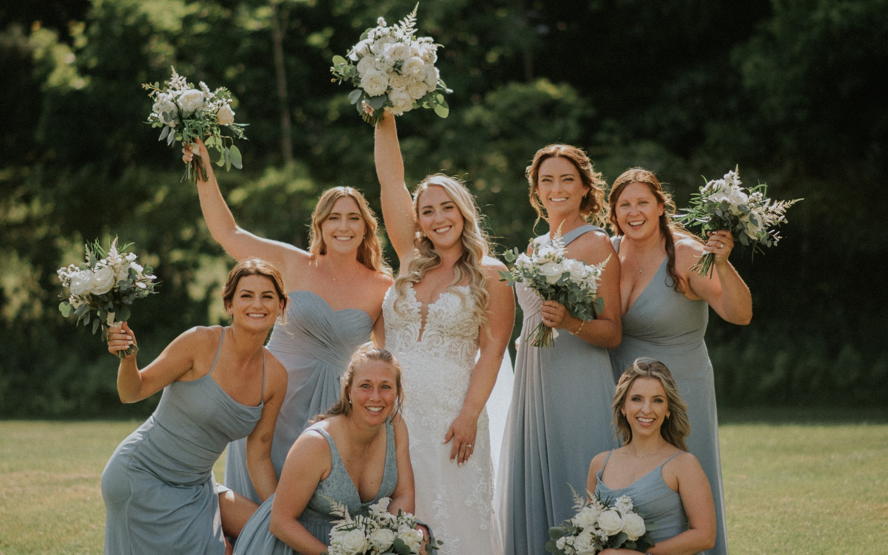 bride and bridesmaids holding flowers. bridesmaids in blue dresses surrounding brides.
