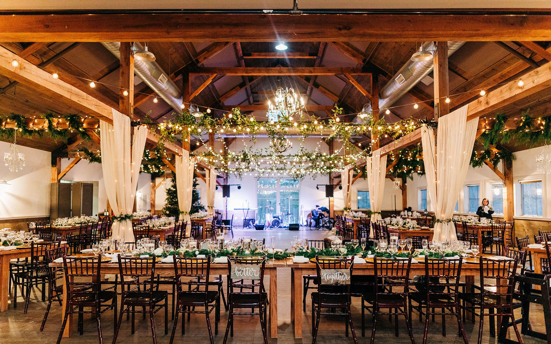 Table with white linens, glassware and floral arrangement centerpiece near other tables under hanging lights in event space at Mountain Top Inn & Resort in Chittenden, VT