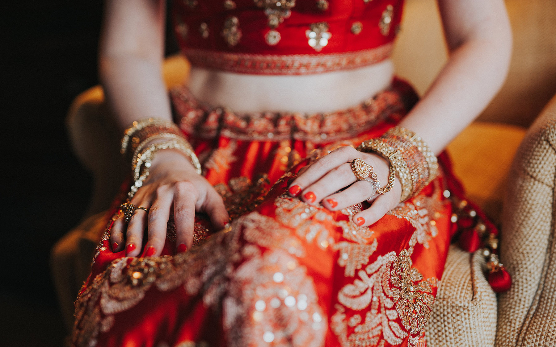 close-up of a woman's waist, arms and lap - dressed in red and gold Indian garb with a bare midrift.