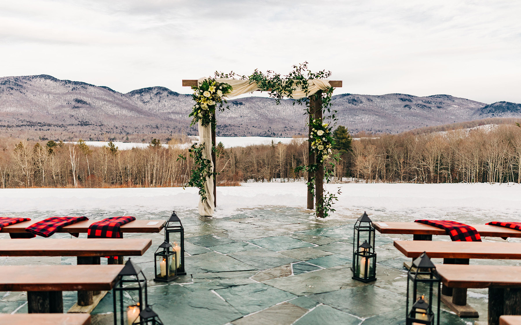 Wedding arch with flowers on it in front of empty seats with scarves and lanterns on seats with snowy mountain in background at Mountain Top Inn & Resort in Chittenden, VT