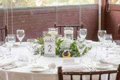 table setting for a summer wedding in a beach pavilion with white linens and simple greenery.