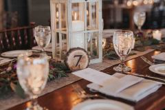 A table set with white lanterns, glassware and place settings.
