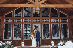 wedding couple kissing on porch of chalet style house with snow all around