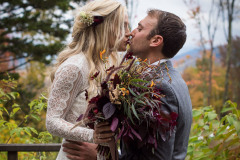 a bride and groom in traditional dress, holding wild fall flowers, kissing.