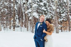 Wedding couple standing in snowy woods embracing