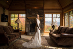 a bride with long blonde hair in a white wedding dress standing in the center of a room with her gown trailing behind her.