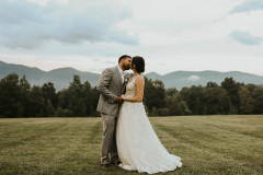 Bride and groom kissing in front of green mountains of vermont. 