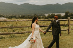 bride and groom in front of wooden fence looking at each other, walking together. mountains and lake in background.