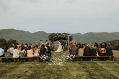 bride and groom at wedding knoll decorated with floral with guests sitting at farmhouse benches with green mountains in the background.