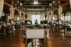event barn decorated with white florals, drapery, and string lights with sweetheart table in the center with a white loveseat.