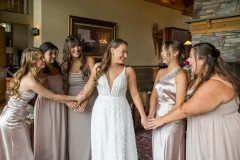 bride in center with bridesmaids holding her hands and smiling at each other.