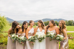 bride and bridal party holding bouquets smiling at each other with mountain scape in the background