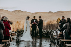 bride and groom in front of ceremony floor florals with officiant with mountains in background during ceremony.