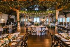 event barn with hanging wisteria and greenery from rafters, and farmhouse tables with greenery and floral arrangements.