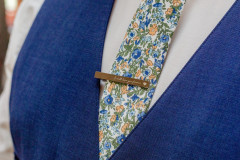 close up of grooms suit featuring a floral tie and a tie clip.