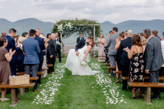 bride and groom kissing halfway down the aisle of a wedding ceremony with mountains in the background.