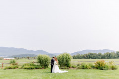 bride and groom standing in front of wooden fence with meadow and mountain scape in background