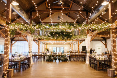 Event barn showcasing lights and greenery, with long farmhouse tables