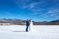 photo of bride and groom on ski hill showcasing mountains behind them in the winter