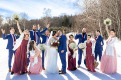 winter wedding featuring bride and groom kissing with bridesmaids and groomsmen around them cheering holding white bouquets