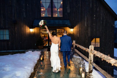 bride and groom in winter walking to dark wooden event barn on path