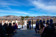 winter wedding on terrace with floral design, featuring bride and groom underneath the arbor, in front of mountains
